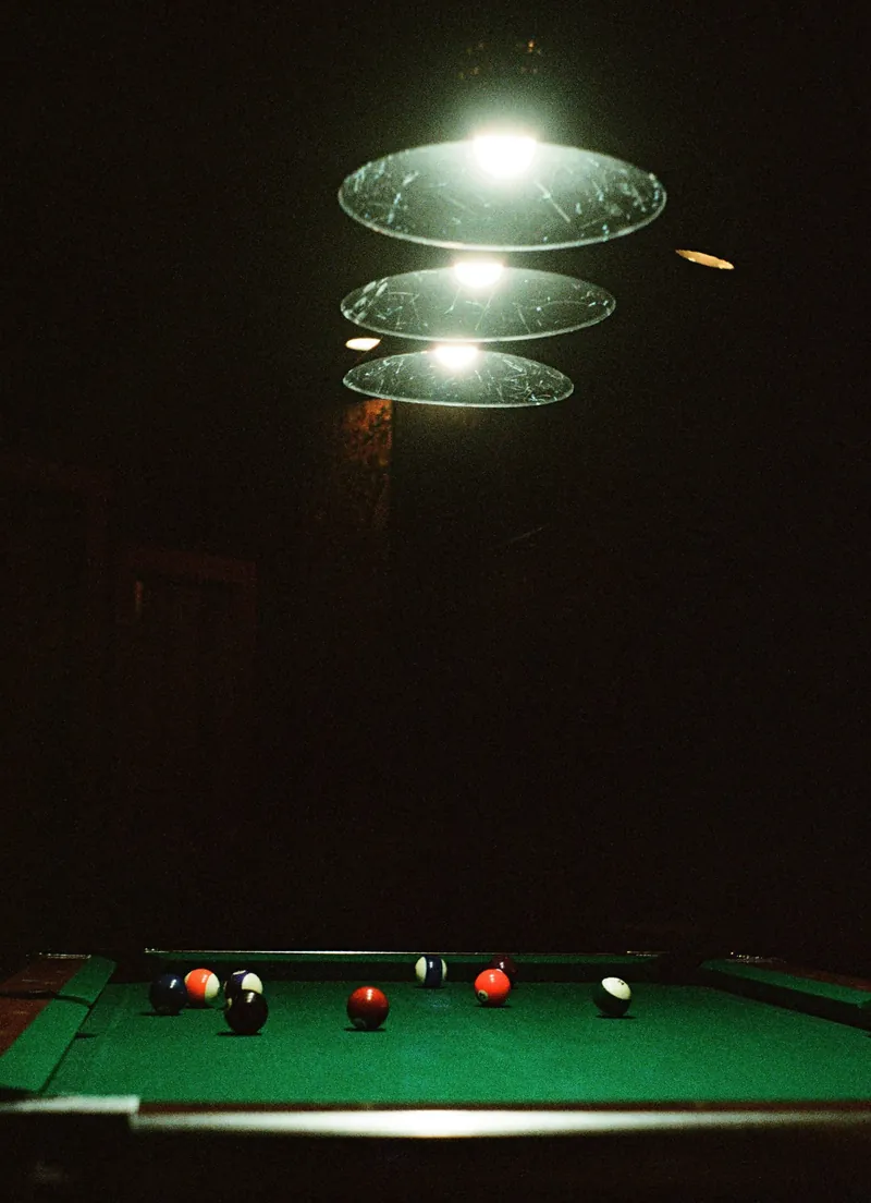 A pool table under a row of glowing pendant lights